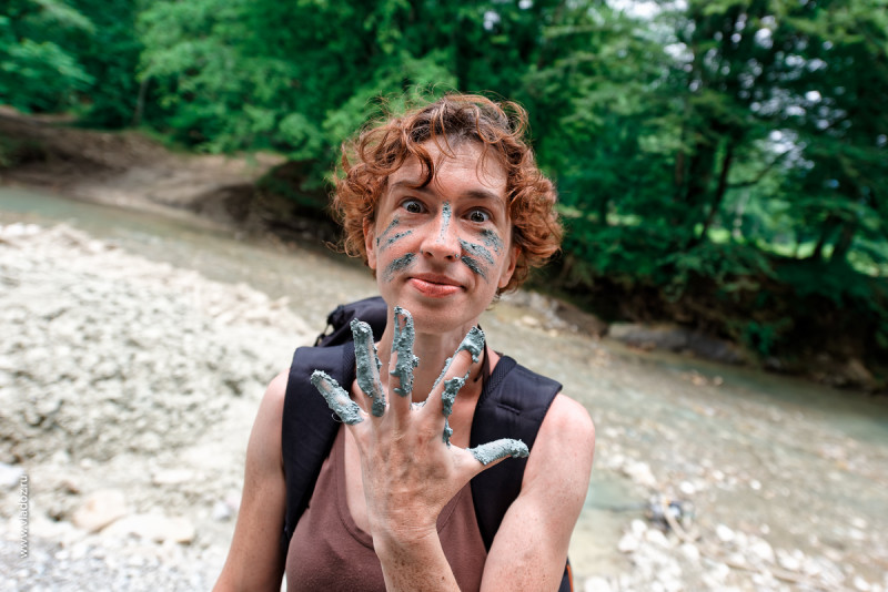 Deposit of blue clay on the Psaho river, Sochi, Russia. Woman is showing hand and face smeared with clay.