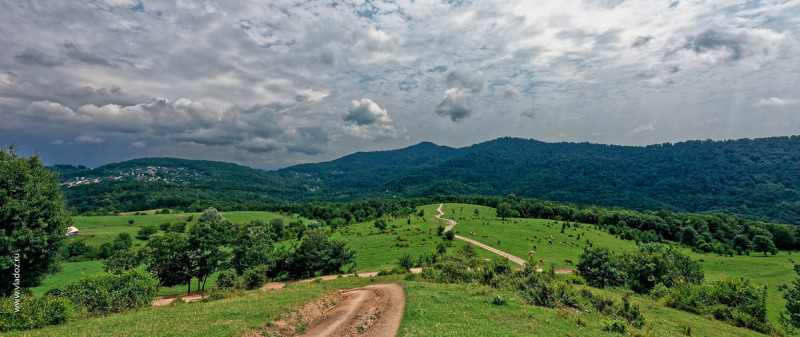 The road up the hillside near the Psaho river, Sochi, Russia. View of green valley on a hot summer day with lots of clouds in the sky.