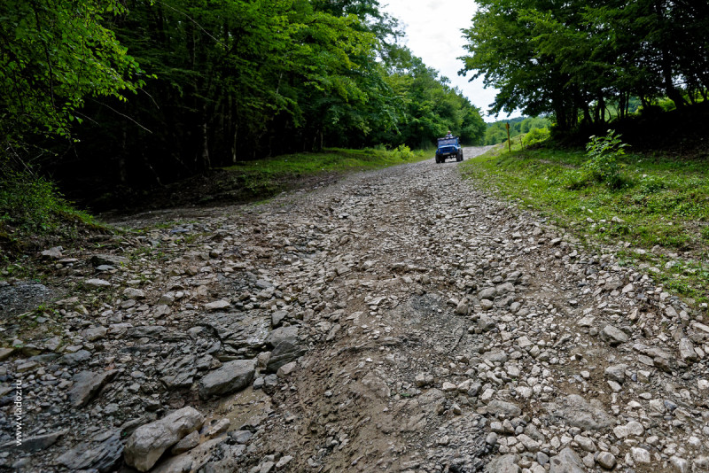 The road up the hillside near the Psaho river, Sochi, Russia. View of green forest on a hot summer day with lots of clouds in the sky. Blue car goes ahead on the stone road.